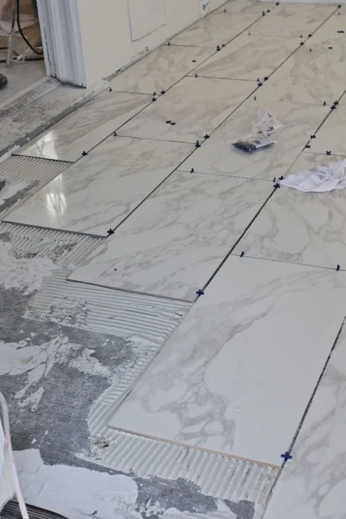 Large marble-look floor tiles set in an offset pattern over combed thin-set with blue leveling clips in Barrhaven, Ottawa