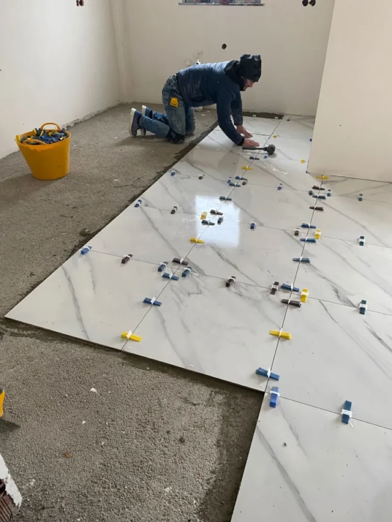 Installer setting large-format marble-look floor tile with a leveling system in Kanata, Ottawa