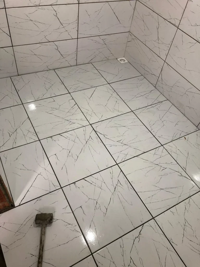 Wet area tiled in glossy white tile with dark veining, with the floor set on the diagonal around a square drain, in Riverside South, Ottawa