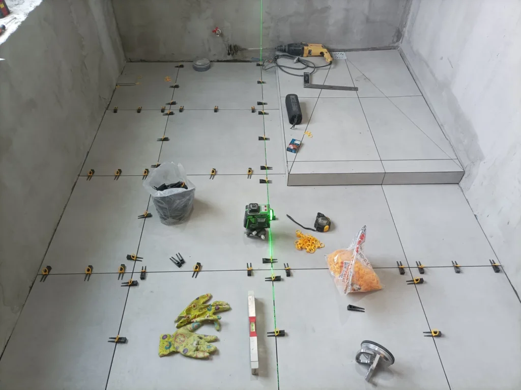 Large grey floor tiles laid out with a cross-line laser level and leveling clips, with a raised tiled step, in Rockland, Ontario