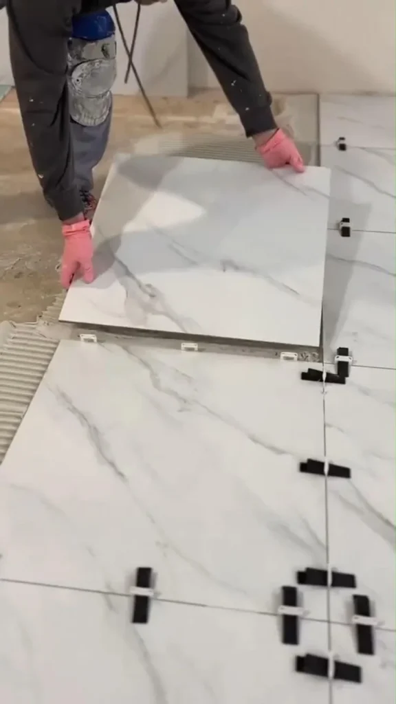 Installer setting a large-format marble-look tile into thin-set with leveling clips in Stittsville, Ottawa